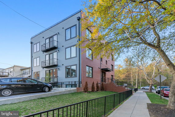 Front view of a modern multi-story apartment building with a combination of red brick and gray paneling.