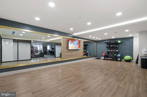 Indoor gym area with wooden flooring, large mirrors, and exercise equipment including weights and stability balls.