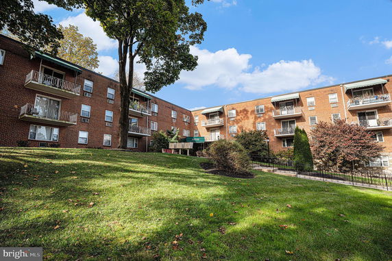 Front view of a multi-story brick apartment building with balconies and a grassy lawn in the foreground.