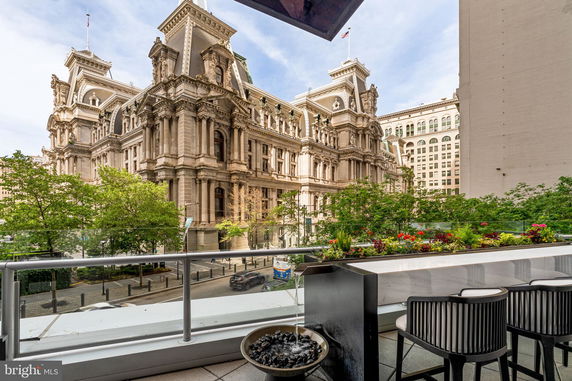Panoramic view from a balcony overlooking an ornate historic building with trees and street below.
