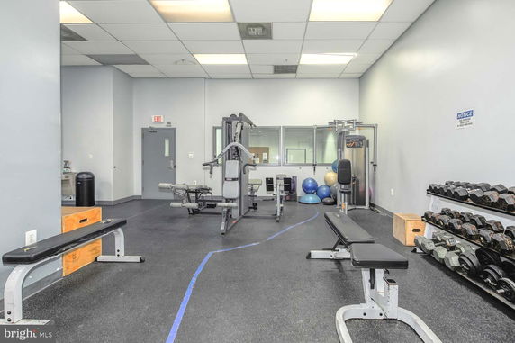 Room with gym equipment and weights, including benches and exercise machines.