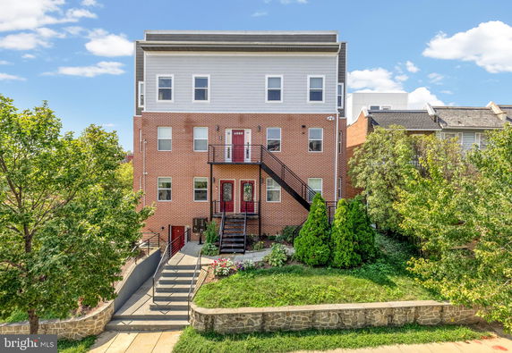 Front view of a multi-story brick building with stairs and landscaping.