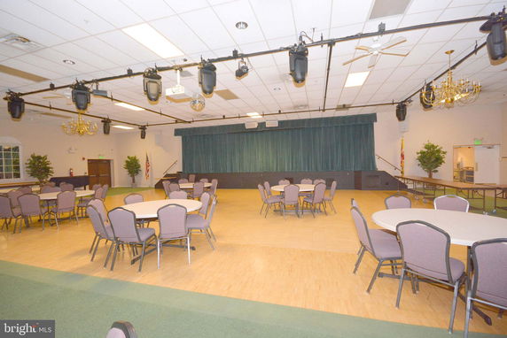 Interior view of a multipurpose room with round tables and chairs, chandeliers, and a stage with curtains.
