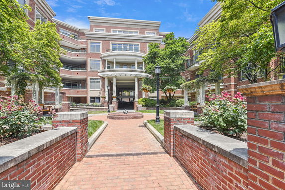Front view of a multi-story brick building with balconies and a landscaped courtyard.