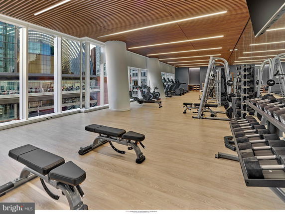 Modern gym area with exercise equipment and large windows with city view.