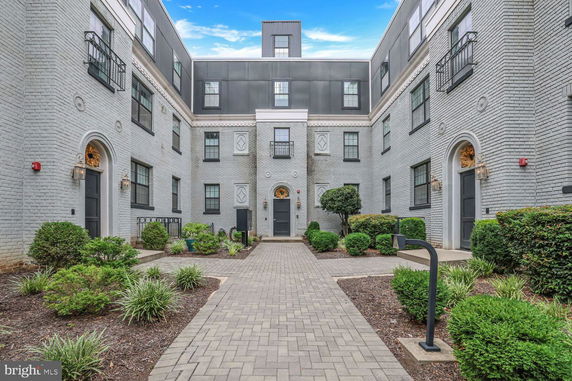 Front view of a multi-story brick building with neatly landscaped pathways and entrance.