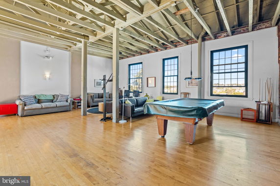 Interior view of a spacious recreational area featuring a pool table, sofas, and large windows.