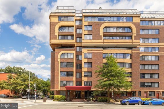 Front view of a multi-story brick apartment building with a red awning entrance.