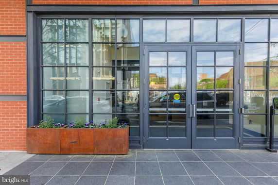 Front view of a building with glass doors and windows, featuring a brick facade and a planter with flowers.