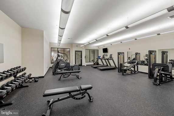 Interior view of a gym with various exercise equipment including treadmills, weight benches, and dumbbells.