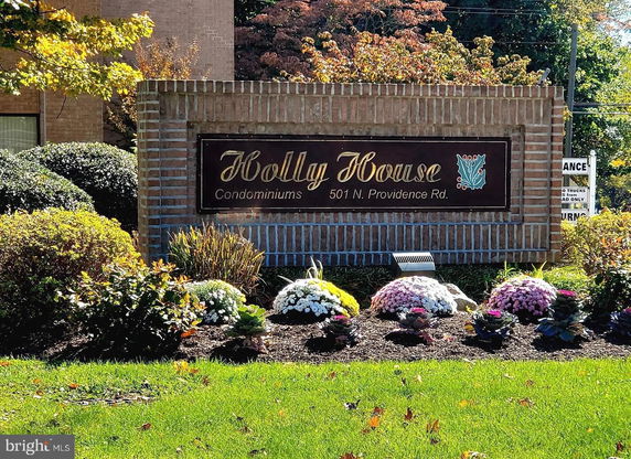 Front view of a condominium sign with brick structure and landscaped surroundings.