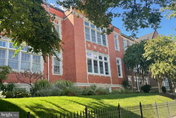 Front view of a large brick building with multiple large windows and a landscaped front yard.