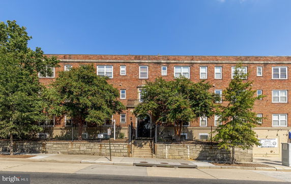 Front view of a multi-story brick building with gated entrance and trees.