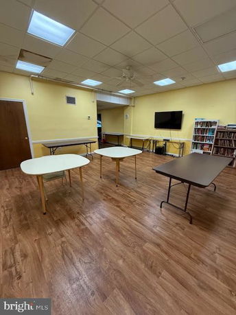 Indoor room with tables, chairs, a TV, and bookshelves on a wooden floor.