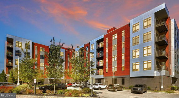 Front view of a modern multi-story apartment building with a parking area and trees in front.