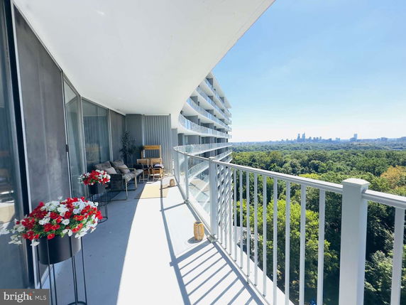 Balcony view from a high-rise building overlooking urban skyline and surrounding green landscape.