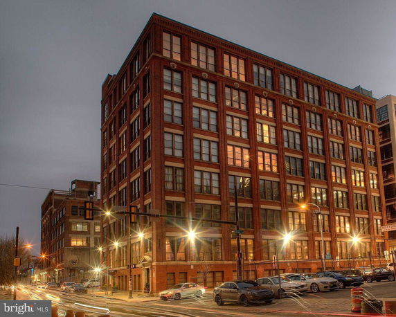 Front view of a multistory brick building at night with several parked cars.