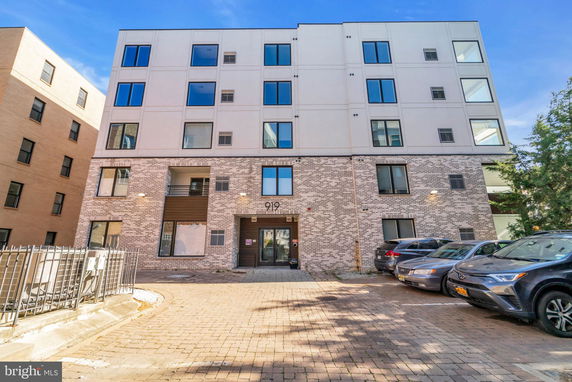 Front view of a multi-story apartment building with a brick facade and parking area.
