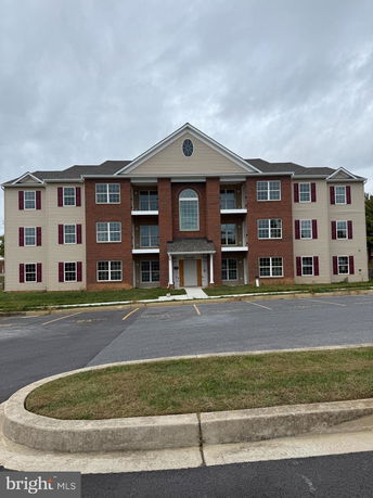 Front view of a three-story apartment building with a central gable and brick facade.