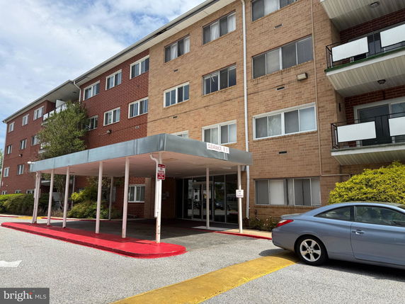 Front view of a multi-story brick apartment building with a covered entrance.