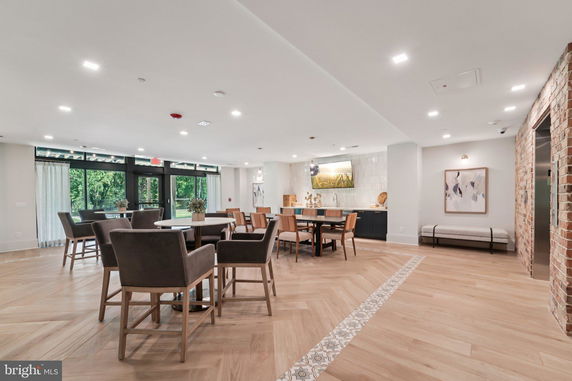 Interior of a clubhouse with tables and chairs, large windows, and decorative art on walls.