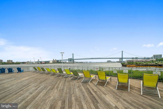 Wide angle view of a deck overlooking a bridge and river, with lounge chairs arranged for seating.