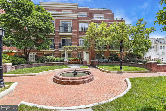 Front view of a multi-story brick building with balconies and landscaped courtyard.