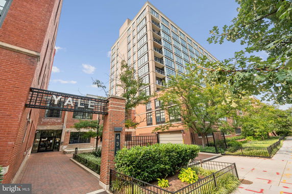 Front view of a multi-story brick building with large windows and a gated entrance.