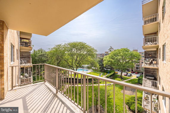 View from a building balcony overlooking greenery, trees, and a swimming pool.