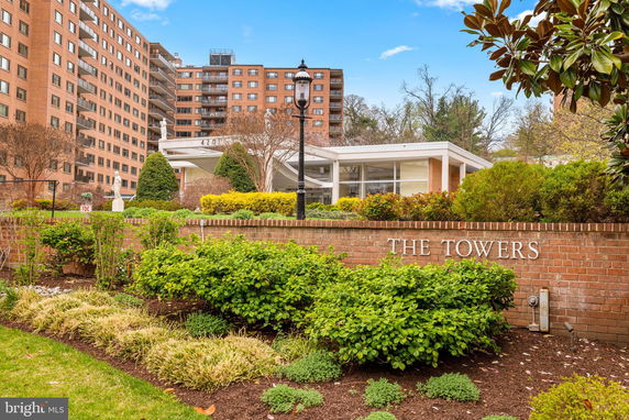 Front view of a tall residential building with a sign reading 'The Towers' and landscaped gardens.