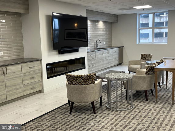 Interior view of a communal space with seating, a wall-mounted TV, a fireplace, and built-in cabinets.