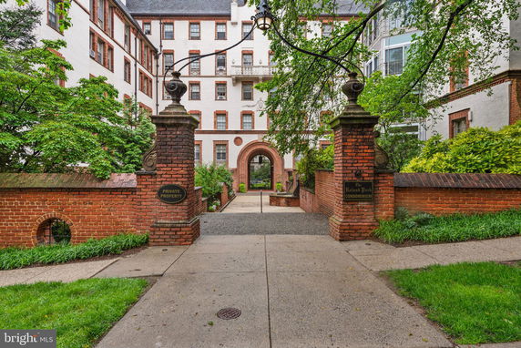 Front view of a multi-story condominium building with brick accents, surrounded by greenery.