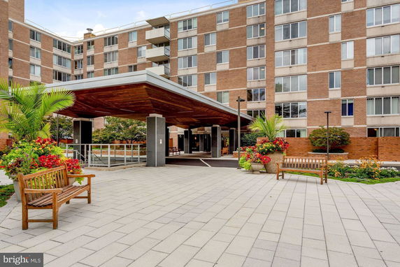 Front view of a multi-story apartment building with an entrance canopy and surrounding landscaped area.