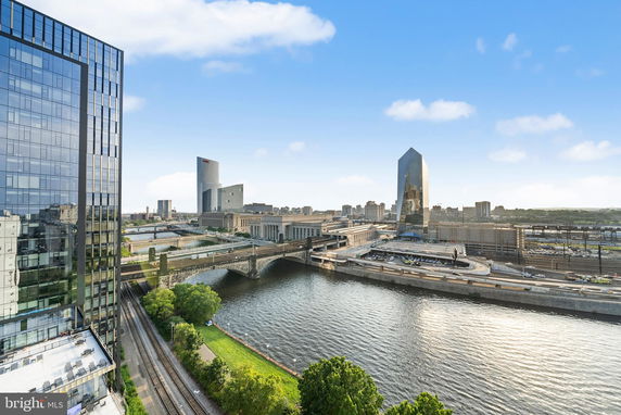 Panoramic cityscape with river, bridges, and tall buildings under a partly cloudy sky.