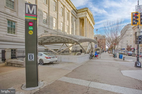 Front view of a large building with a covered metro entrance and a parking area.