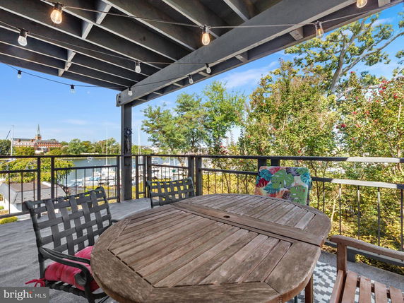 Outdoor patio area with a wooden dining table and chairs overlooking a marina and trees.