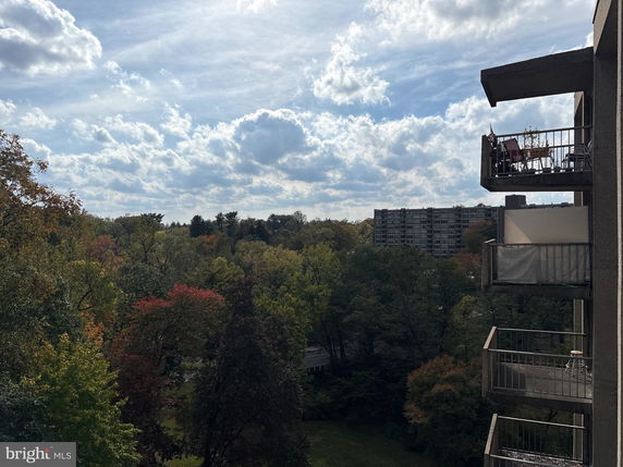 Wide angle view of a building with balconies overlooking a wooded area and cloudy sky.