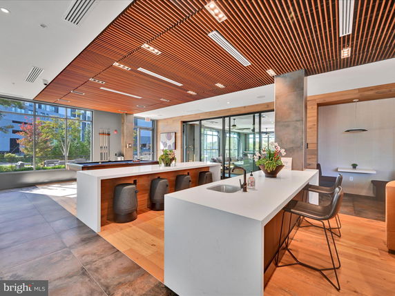 Modern club house interior with a central bar area, seating, and large windows.