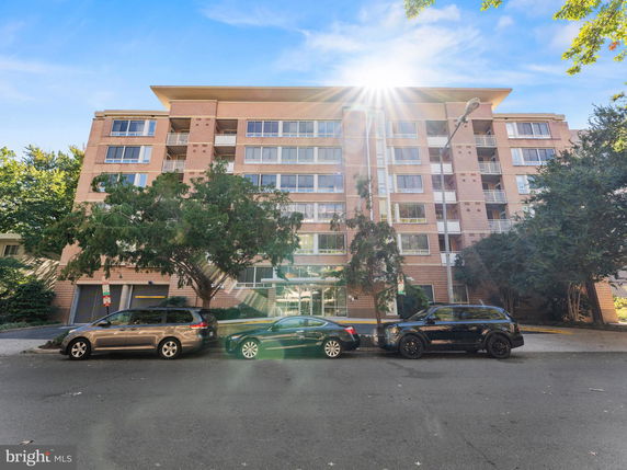 Front view of a multi-story apartment building with balconies and parking spaces in front.