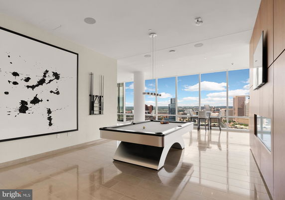 Interior room with a modern pool table, large abstract artwork, and panoramic windows showing city views.