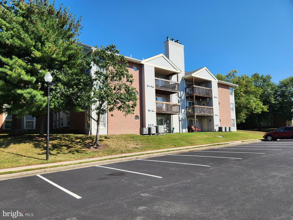 Front view of a multi-story apartment building with balconies and parking area.