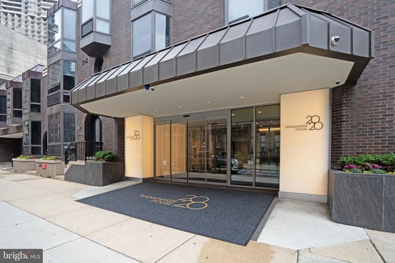 Front view of a modern apartment building entrance with large glass doors and decorative metal structures.