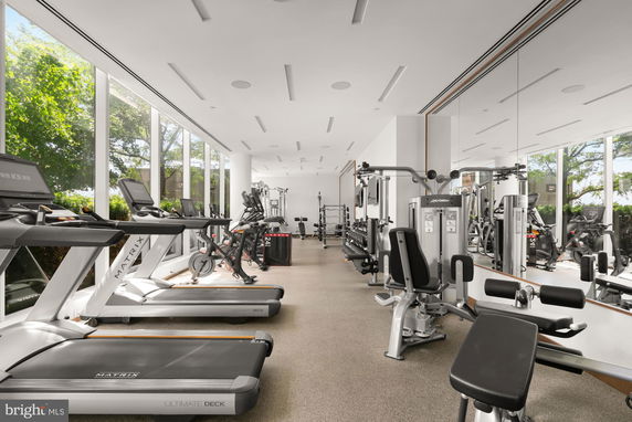Interior view of a gym with various exercise equipment and large windows.
