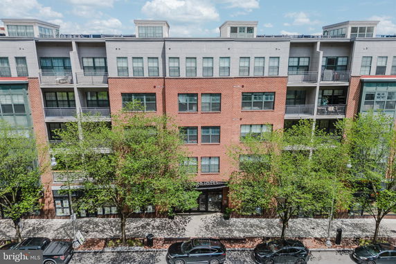 Front view of a multi-story building with a mix of brick and concrete facade, featuring balconies and large windows.