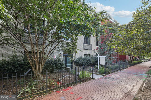 Front view of a multi-story brick building with a sidewalk and trees.