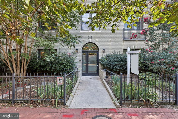 Front view of a multi-story brick building with an arched entrance and wrought iron fence.