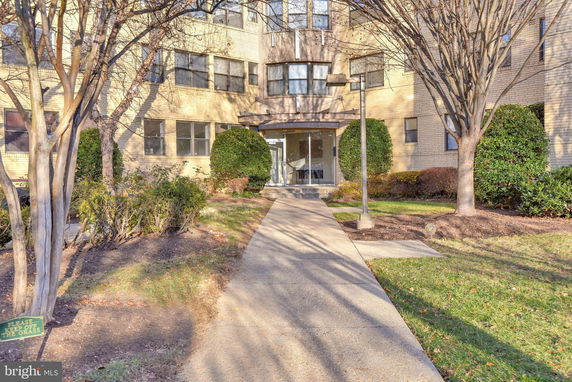 Front view of a multi-story building with a glass entrance and surrounding shrubs.