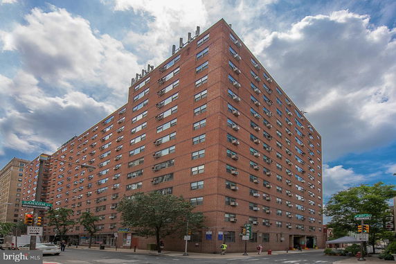 Front view of a multi-story brick apartment building on a city street corner.