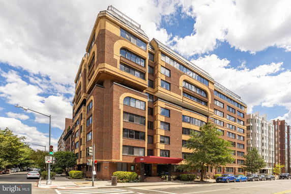 Front view of a multi-story brick building with large windows and a red canopy above the entrance.