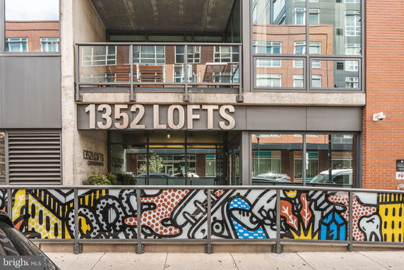 Front view of a modern loft building with large glass windows and colorful graffiti on the lower facade.